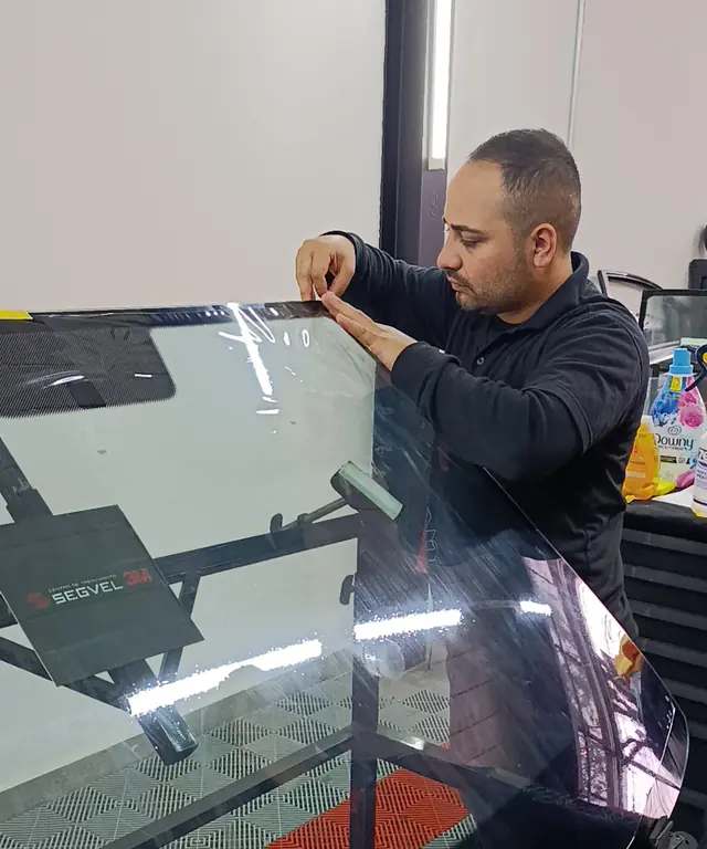 Aplicador instalando película automotiva em um para-brisa, com placa Segvel 3M na bancada